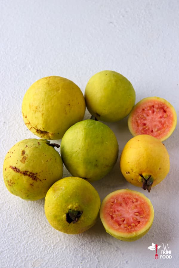 6 guavas and 2 pink guava halves on white backdrop