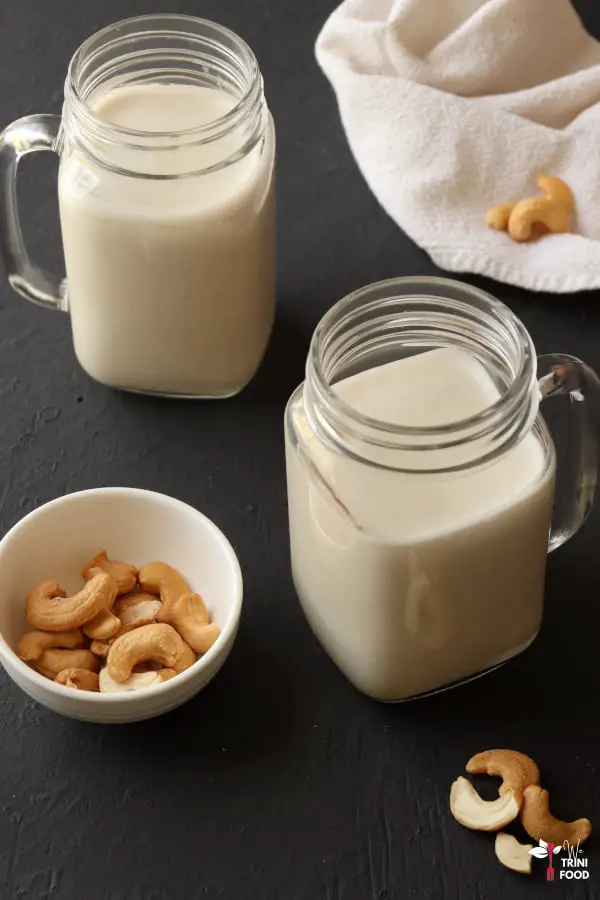 cashew milk in two mason jugs with cashews on the sides on a black background