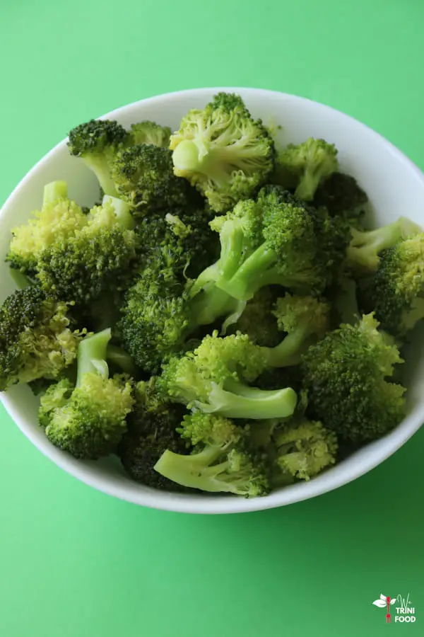 sauteed broccoli in white bowl on green background