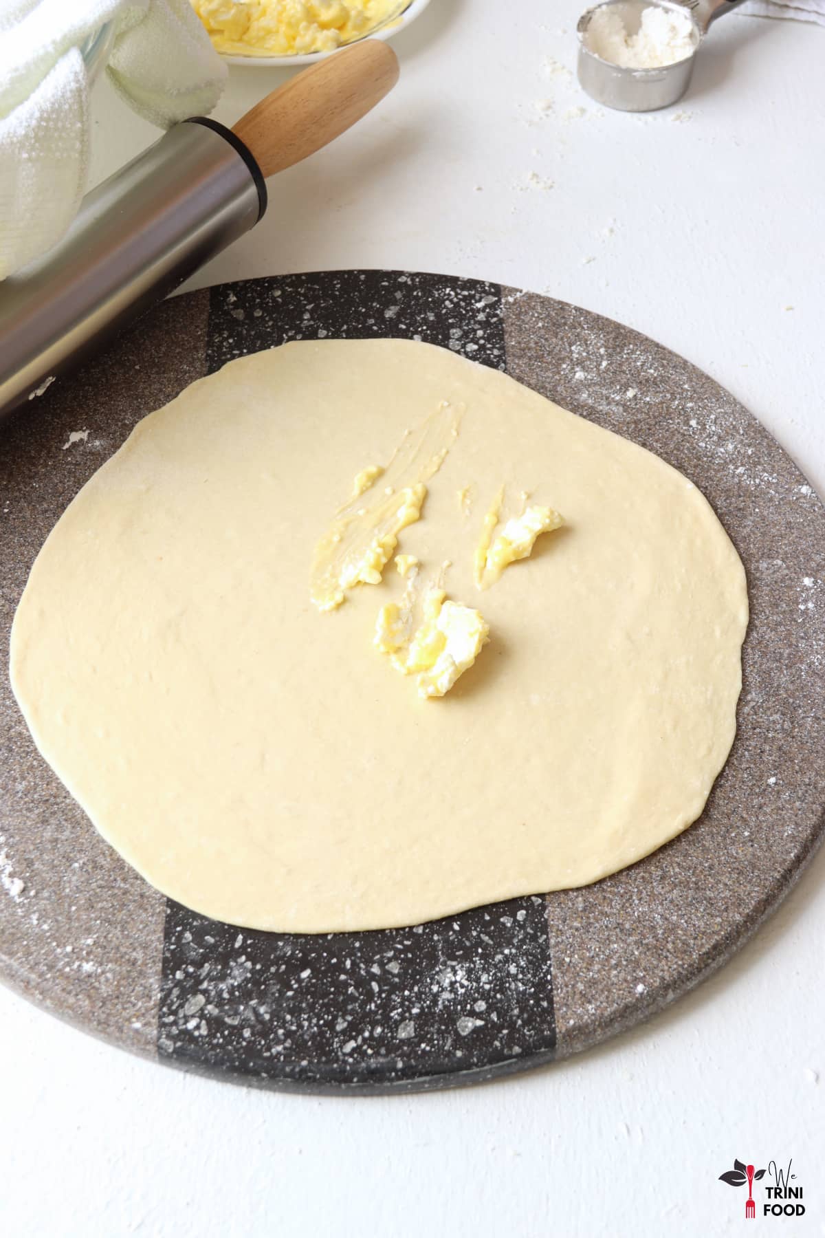 rolled out roti dough with butter and shortening mixture added on top with the rolling pin on the side