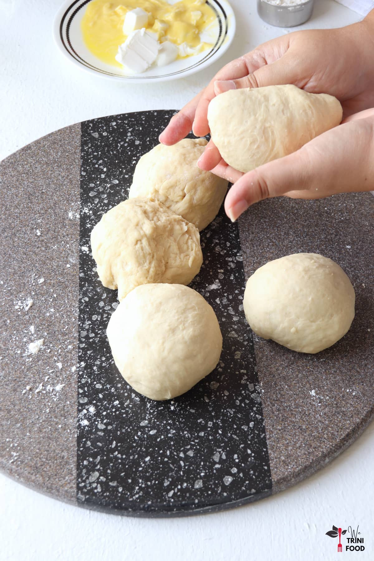 shaping the divided dough into balls with a grey granite background and butter and cookeen in a small plate on the side