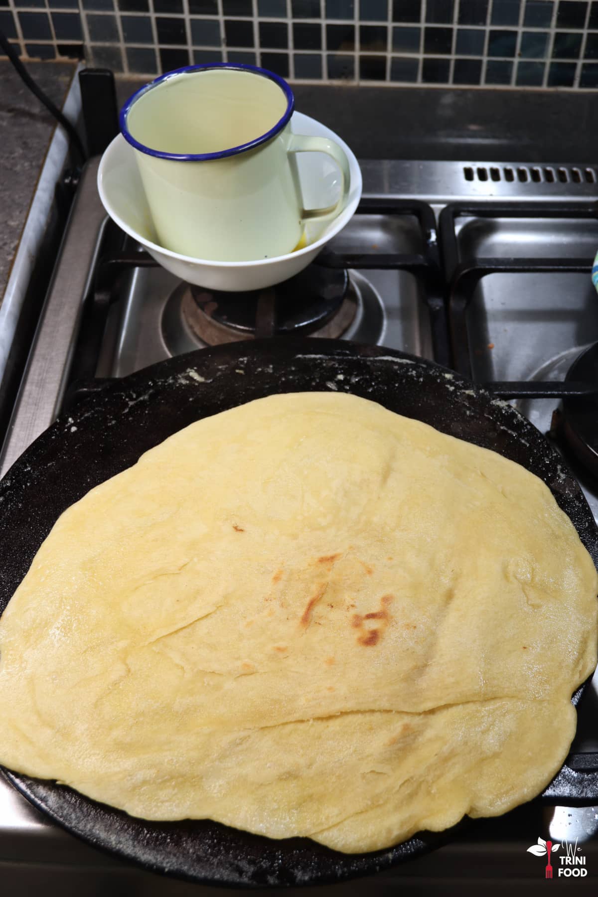 flipped paratha roti on cast iron tawa with a bowl of butter with an enamel cup on the side