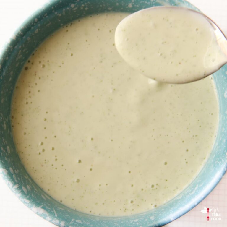 trini garlic sauce in a blue bowl with a spoon with garlic sauce on it with a white background