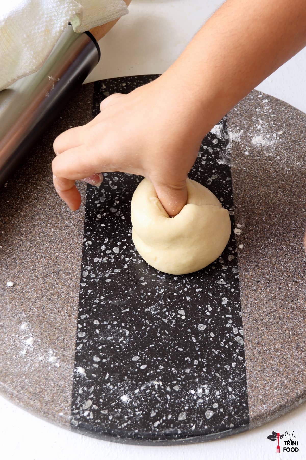 pressing down into the buss up shut roti dough with your thumb with a rolling pin on the side