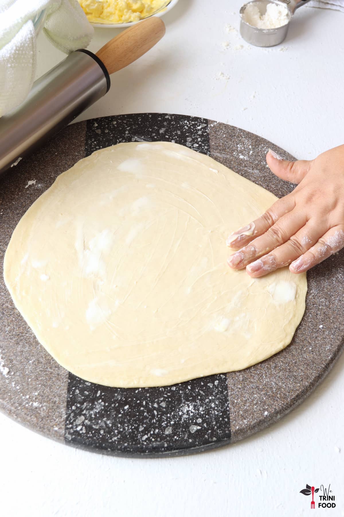 butter and shortening rubbed on the rolled out roti dough with rolling pin and flour on the side