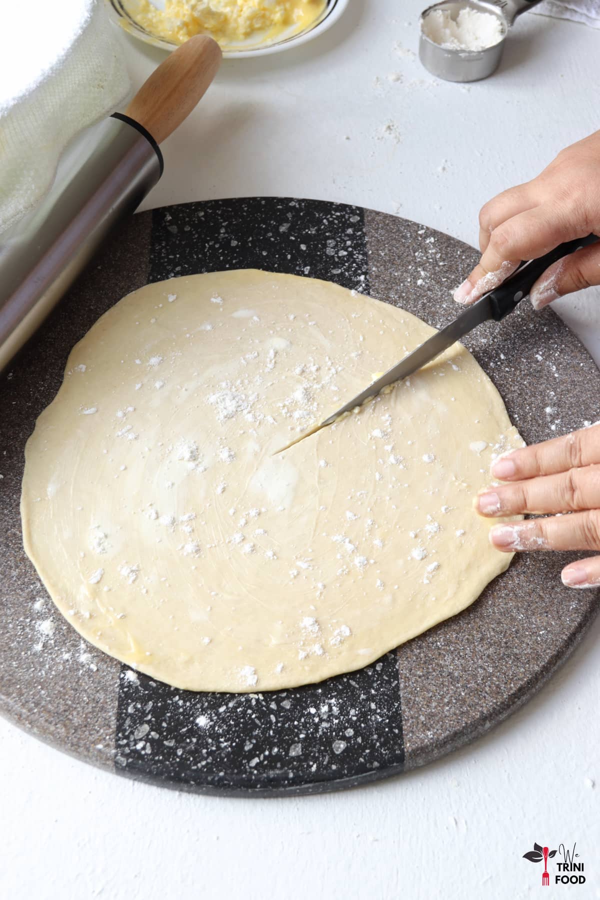 slicing the buttered and floured paratha roti for rolling with the rolling pin, flour and butter in the background