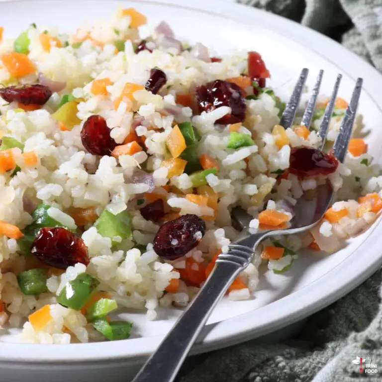 trinidad christmas rice with white rice, red cranberries, chopped green bell pepper and chopped carrots on white plate with silber fork over a green cloth