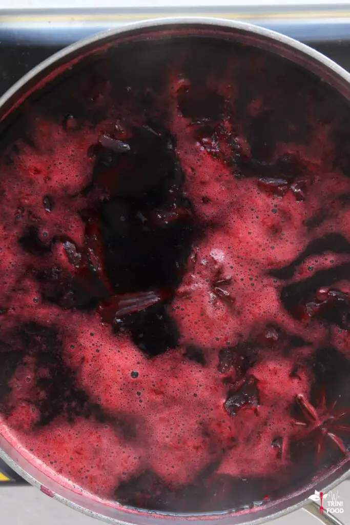 brewing sorrel drink showing dark red lather on the surface of the water in the pot
