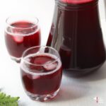 sorrel drink featured image - 2 glasses of sorrel drink with ice and a jug of sorrel with a small christmas tree leaf