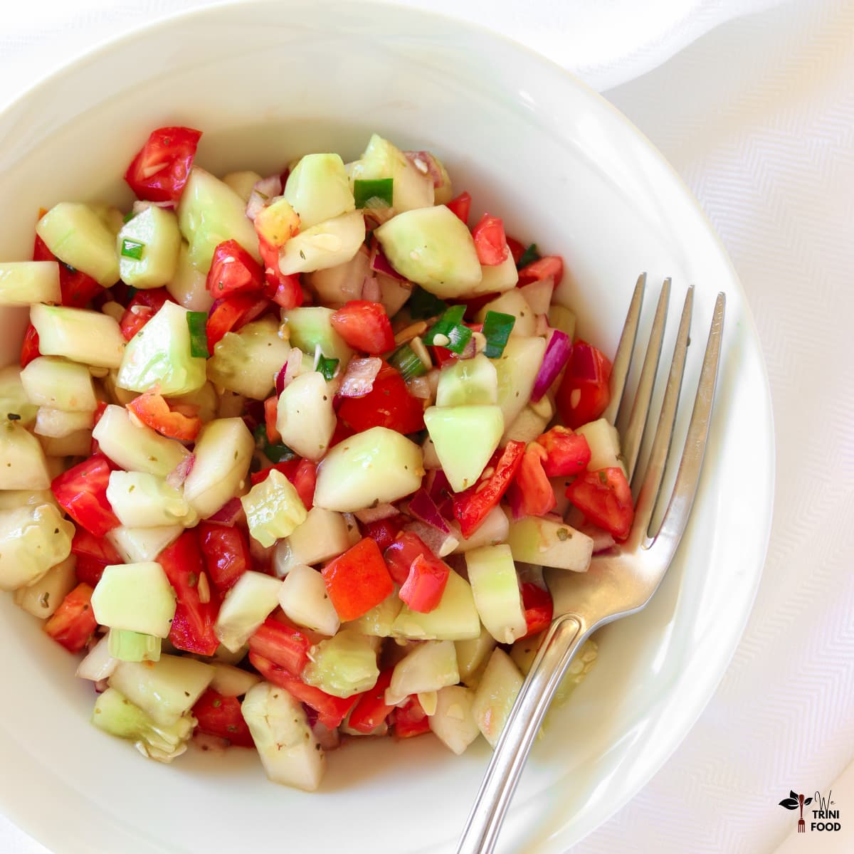 cucumber tomato salad in white bowl with fork