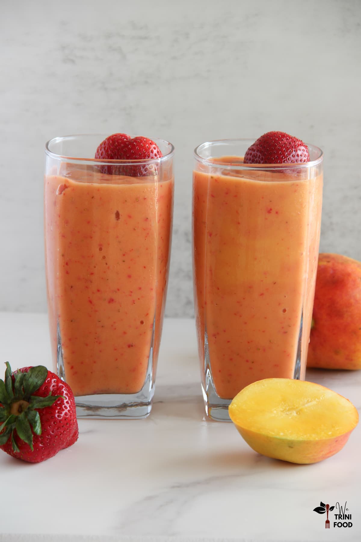 2 glasses of strawberry mango smoothie side by side with ingredients around the glasses