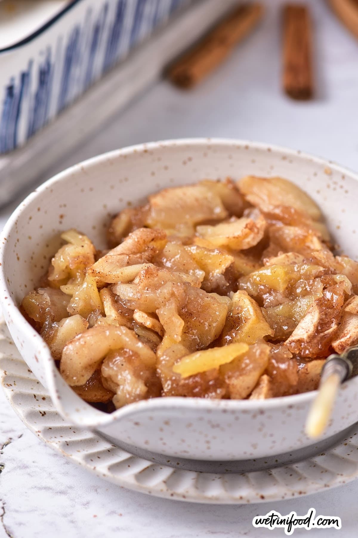 baked apples served in a beautiful white bowl with baking dish in background
