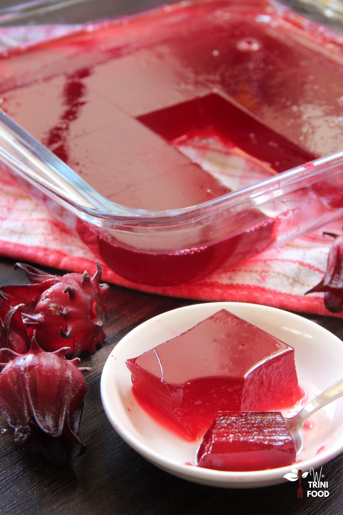 Sorrel jelly in a mini plate and spoon with roselle on the side and sorrel jelly in background
